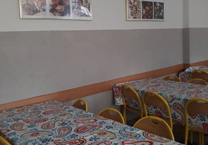 Zdjęcie stołu na stołówce, na ścianie kolorowe obrazy.