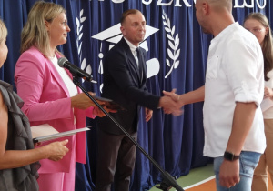 Dyrektor Biura Edukacji wręcza rodzicowi lisy gratulacyjny.